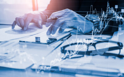 A person is diligently working at a desk with papers, a smartphone, and eyeglasses. Overlaid financial graphs suggest analysis or trading in progress. The scene is illuminated with a blue tint, highlighting themes of asset protection and strategic estate planning.