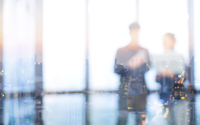 Blurred silhouettes of two people, perhaps discussing estate planning strategies, stand in an office with large windows. The cityscape at dusk overlays them as the bright light from outside creates a dreamy, abstract effect.