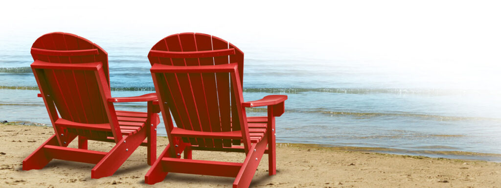 Two red Adirondack chairs are perfectly positioned on a sandy beach, facing the gentle waves of the ocean under a clear sky, offering an ideal spot to ponder your next Roth IRA withdrawals.