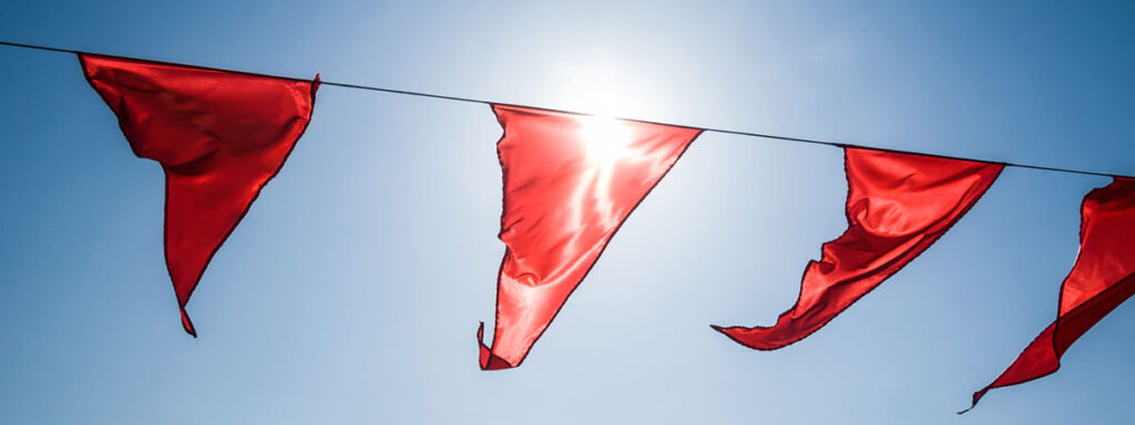 Red triangular flags dangle on a string against a clear blue sky, with the sun illuminating them brightly, much like red flags in a tax audit catching the eye.