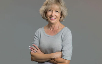 Head shot of middle-aged block woman wearing a casual grey blouse with her arms crossed. She is smiling.